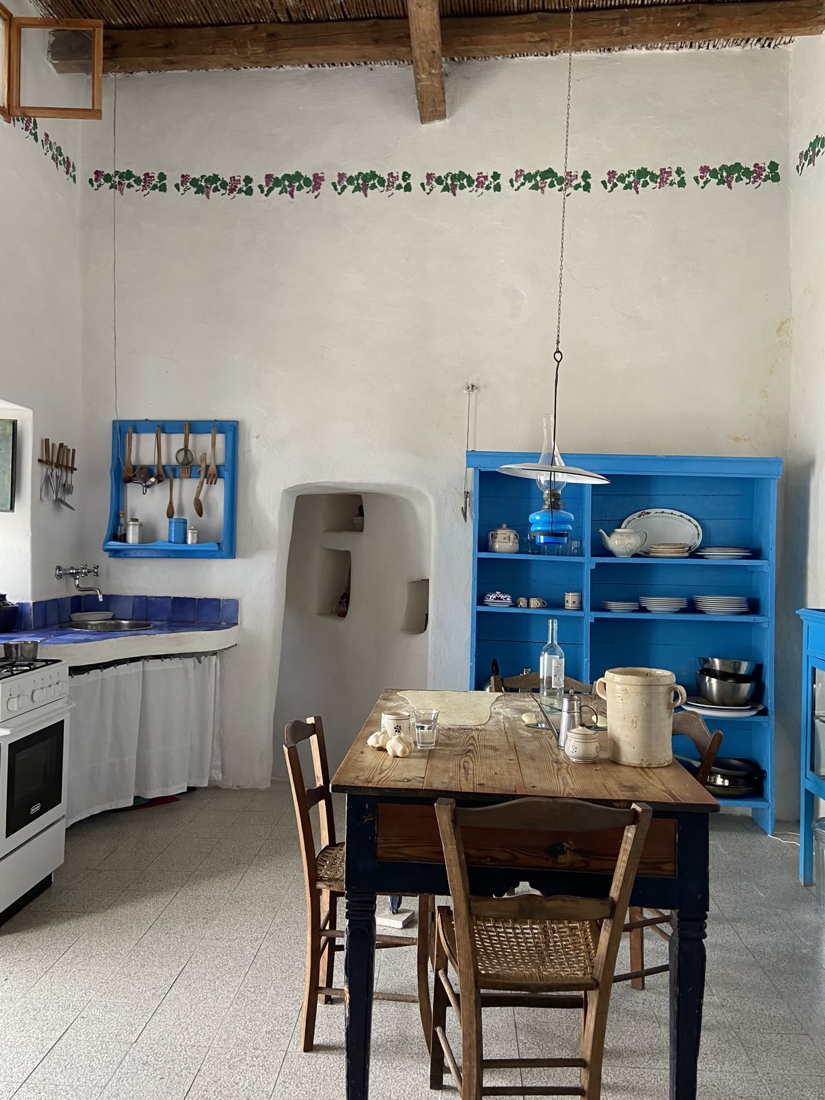 Whitewashed island kitchen with a blue dresser, wooden table and hand-painted vine border