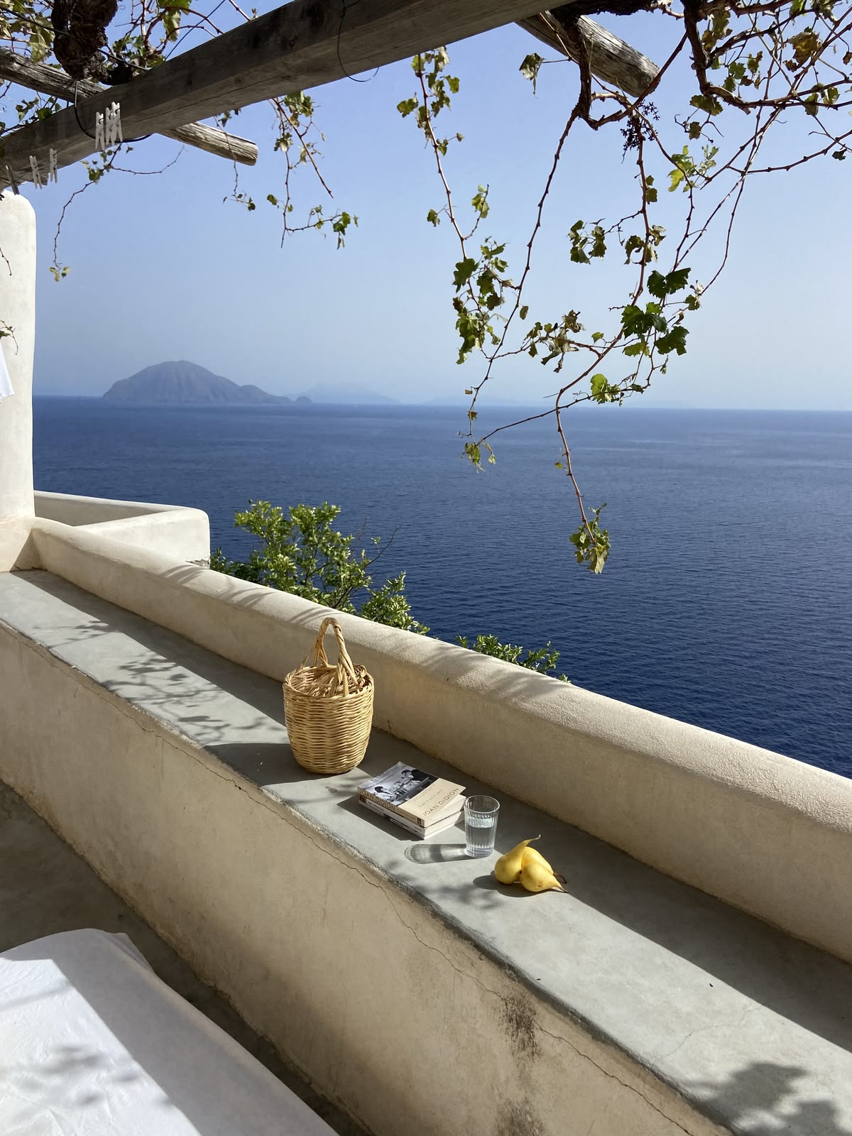 Sunlit terrace overlooking the sea with a woven basket, book and glass of water